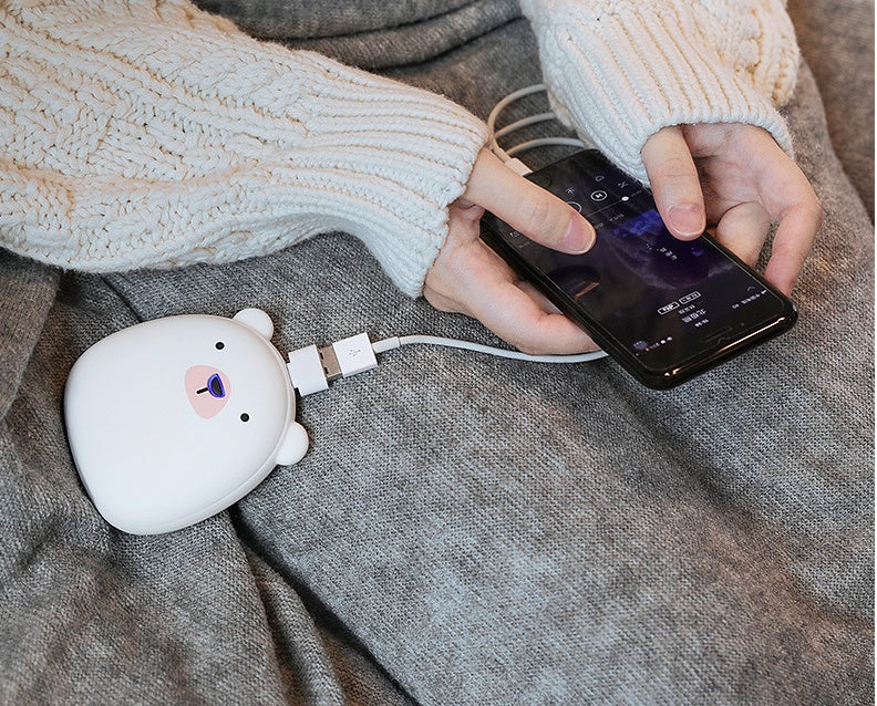 Polar bear USB Rechargeable Hand Warmer charging a smartphone, showcasing dual functionality for outdoor convenience.