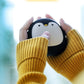Person holding penguin USB Rechargeable Hand Warmer with both hands, great for staying warm during outdoor activities.
