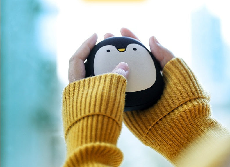 Person holding penguin USB Rechargeable Hand Warmer with both hands, great for staying warm during outdoor activities.