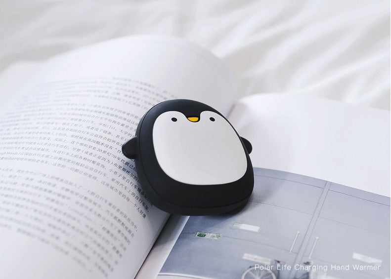 Penguin-shaped USB Rechargeable Hand Warmer resting on an open book, combining warmth and adorable design for camping use.