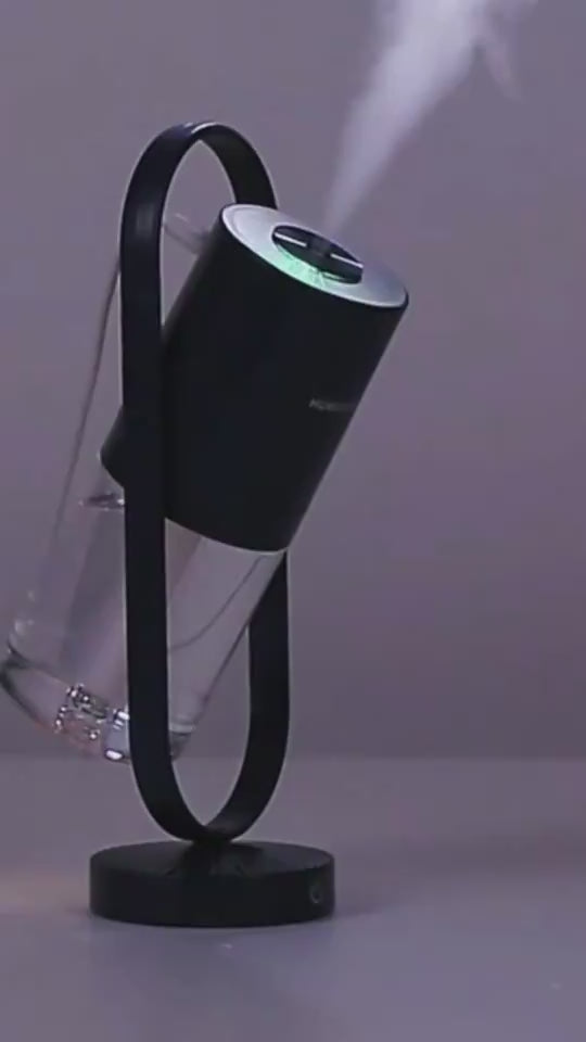 Sleek black USB Mini Humidifier in a tilted stand, releasing visible mist, rechargeable and perfect for modern home or workspace.